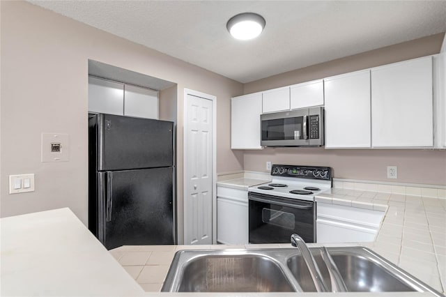 kitchen featuring sink, range with electric stovetop, black refrigerator, and white cabinetry