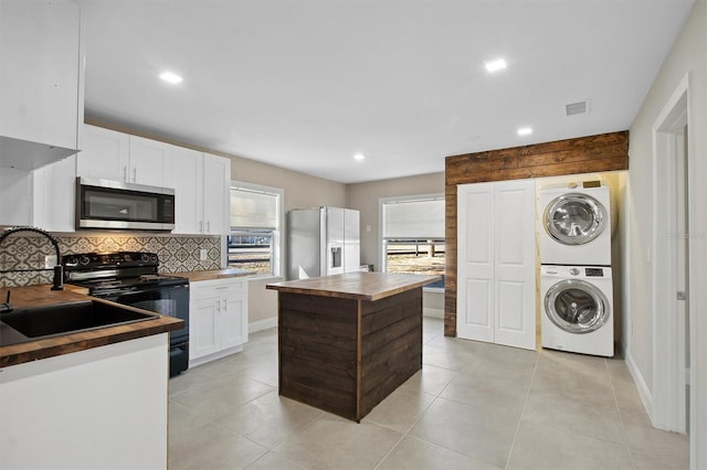 kitchen featuring stainless steel appliances, white cabinetry, stacked washer / dryer, tasteful backsplash, and a kitchen island