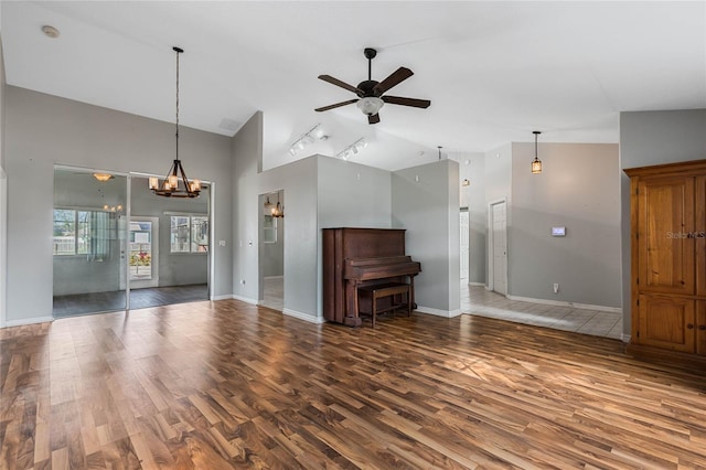 unfurnished living room with ceiling fan with notable chandelier, dark hardwood / wood-style flooring, track lighting, and vaulted ceiling