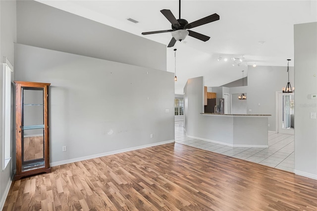 unfurnished living room featuring light hardwood / wood-style floors, ceiling fan with notable chandelier, and vaulted ceiling