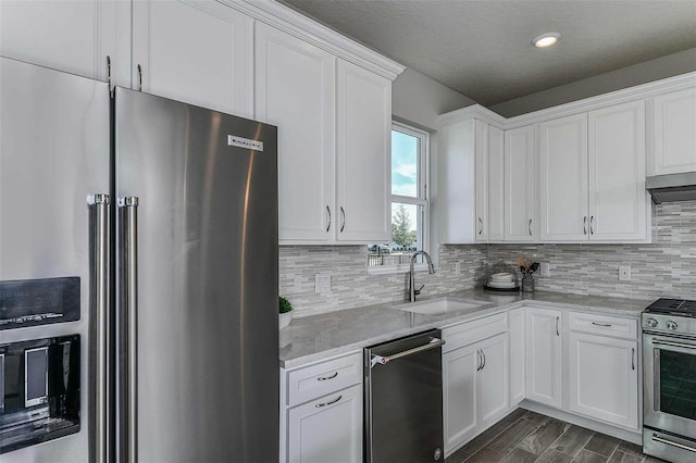 kitchen featuring appliances with stainless steel finishes, light stone countertops, range hood, white cabinets, and sink