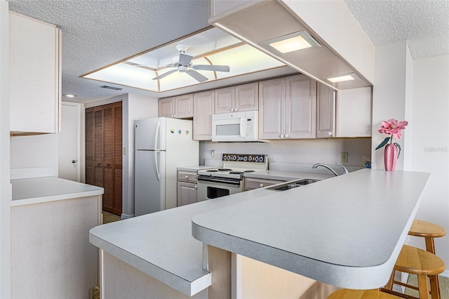 kitchen featuring ceiling fan, kitchen peninsula, sink, white appliances, and a kitchen breakfast bar