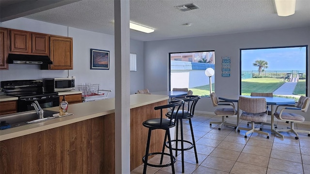 kitchen with electric range, sink, a kitchen breakfast bar, a textured ceiling, and light tile patterned floors