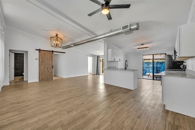 unfurnished living room featuring a barn door, plenty of natural light, ceiling fan with notable chandelier, and light hardwood / wood-style floors