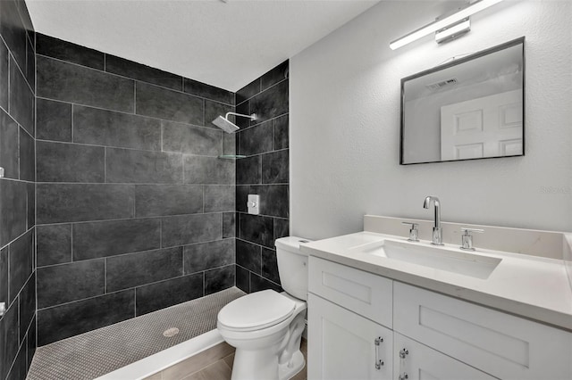 bathroom featuring toilet, vanity, a tile shower, and tile patterned flooring