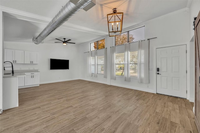 unfurnished living room featuring a barn door, a high ceiling, light hardwood / wood-style flooring, ornamental molding, and ceiling fan with notable chandelier