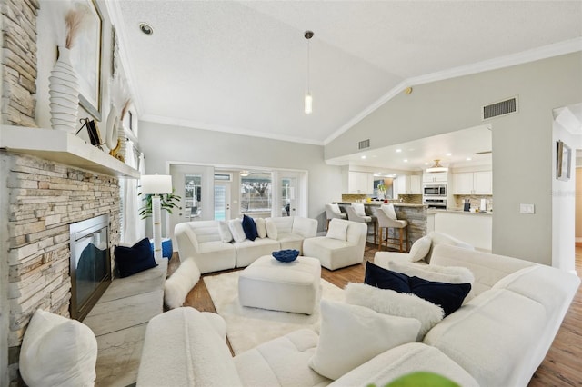 living room featuring vaulted ceiling, a fireplace, ornamental molding, and light hardwood / wood-style floors