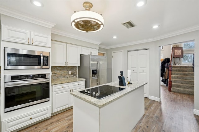 kitchen with light hardwood / wood-style floors, stainless steel appliances, white cabinets, a kitchen island, and light stone counters