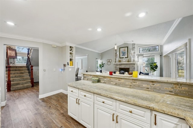 kitchen featuring crown molding, vaulted ceiling, light stone counters, and white cabinetry