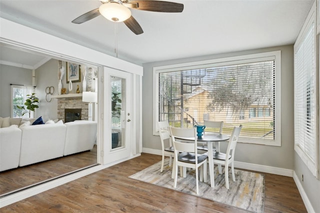 dining area featuring ceiling fan, a stone fireplace, ornamental molding, and hardwood / wood-style floors