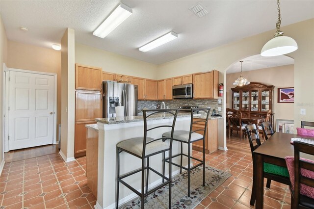 kitchen featuring a breakfast bar area, hanging light fixtures, appliances with stainless steel finishes, backsplash, and a center island