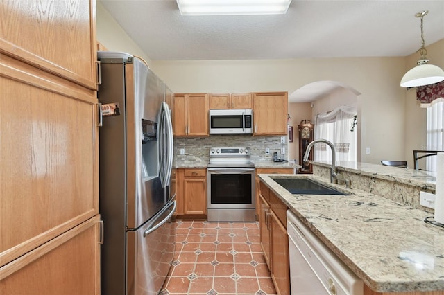 kitchen with a sink, tasteful backsplash, stainless steel appliances, light tile patterned flooring, and hanging light fixtures