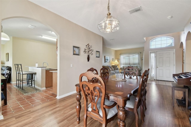 dining room featuring visible vents, arched walkways, light wood finished floors, and baseboards