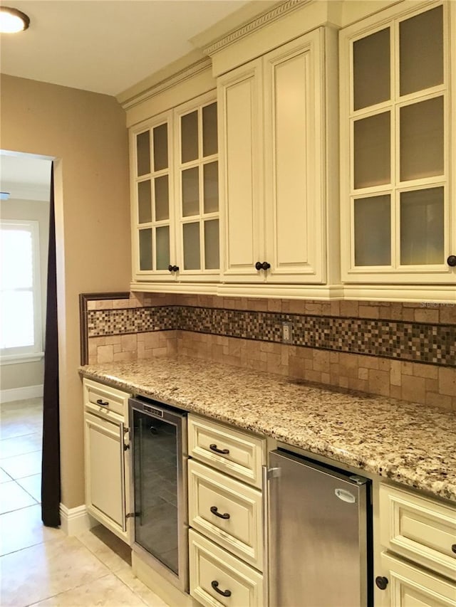 kitchen with light stone countertops, beverage cooler, decorative backsplash, cream cabinets, and light tile patterned flooring