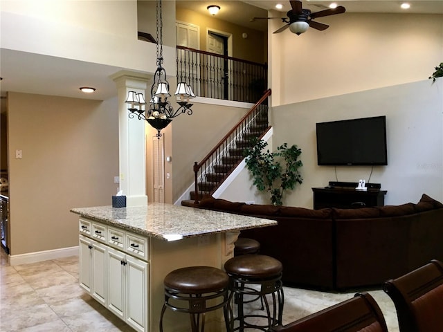 kitchen with hanging light fixtures, white cabinets, a high ceiling, light stone countertops, and a center island