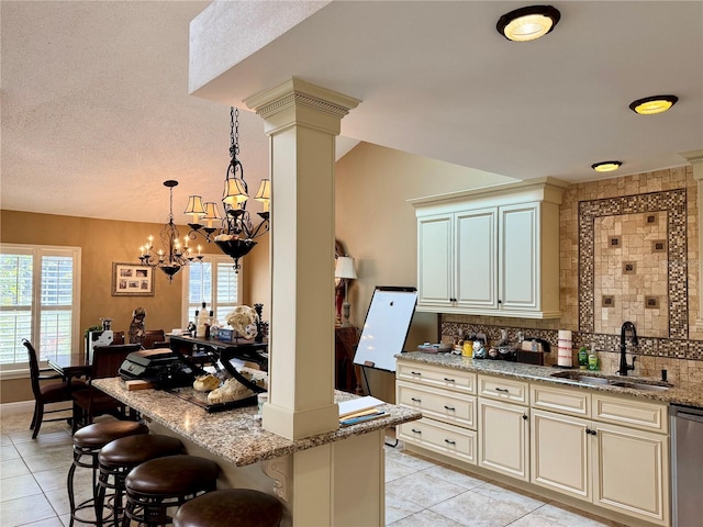 kitchen featuring a breakfast bar, sink, light stone counters, stainless steel dishwasher, and cream cabinets