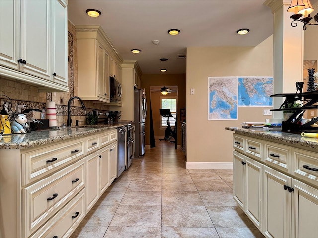 kitchen featuring sink, light stone counters, stainless steel appliances, cream cabinets, and backsplash