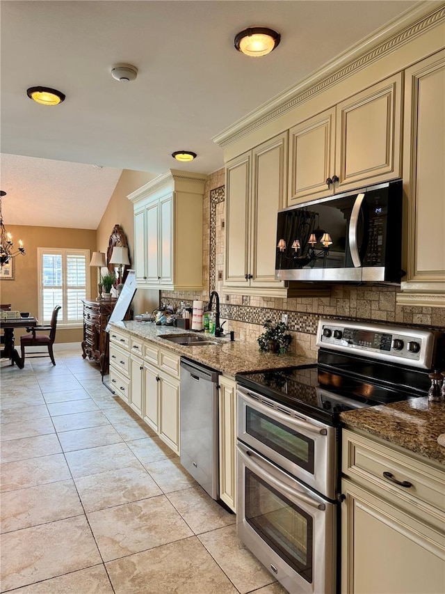 kitchen featuring sink, stone counters, stainless steel appliances, decorative light fixtures, and cream cabinetry