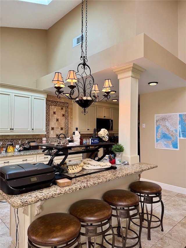 kitchen featuring a towering ceiling, light stone countertops, a breakfast bar area, and ornate columns