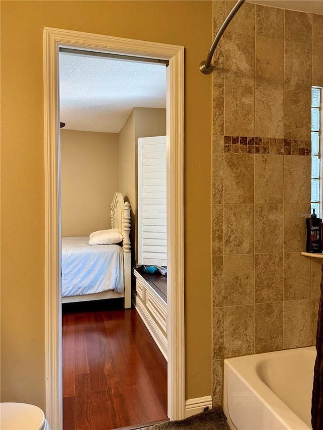 bathroom featuring hardwood / wood-style flooring, tiled shower / bath, and toilet