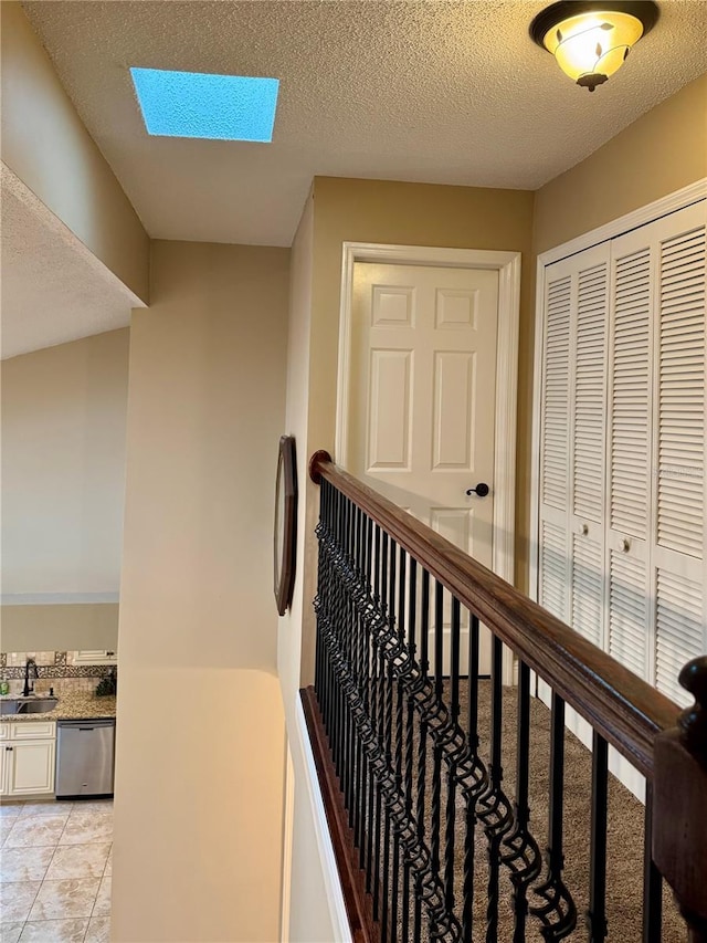 hallway featuring a skylight, sink, a textured ceiling, and light tile patterned floors