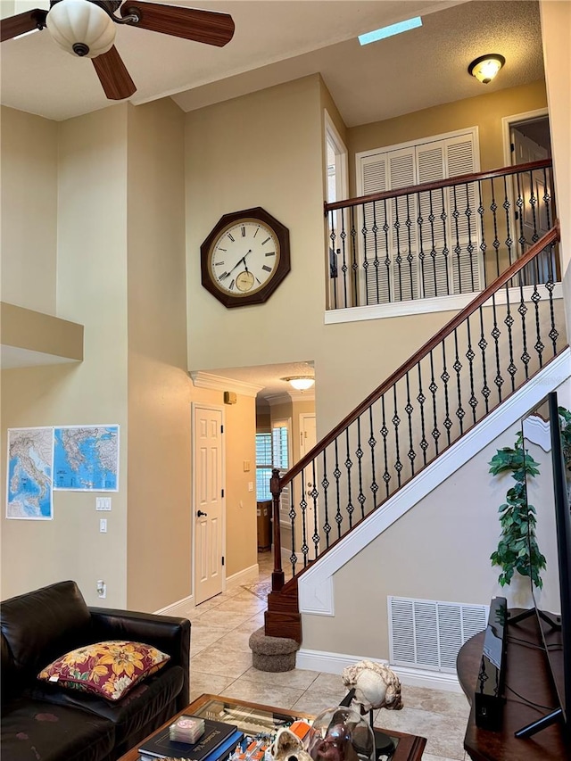 living room with a towering ceiling, ceiling fan, and light tile patterned flooring