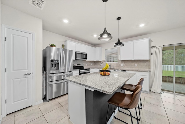 kitchen featuring appliances with stainless steel finishes, white cabinetry, a center island, light stone counters, and decorative backsplash