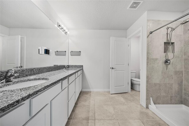 bathroom with vanity, a textured ceiling, toilet, and a tile shower