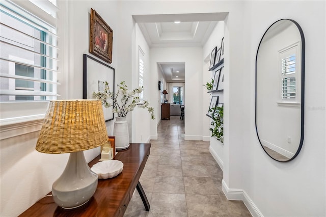 corridor with a raised ceiling, light tile patterned flooring, and crown molding