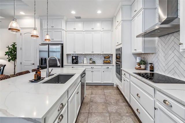 kitchen featuring sink, white cabinets, wall chimney range hood, pendant lighting, and appliances with stainless steel finishes