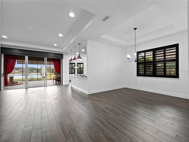 unfurnished living room featuring a chandelier, a tray ceiling, and dark hardwood / wood-style flooring