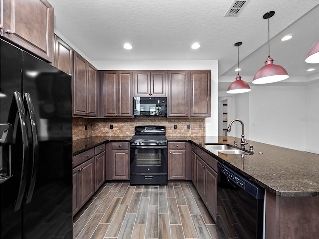 kitchen featuring decorative light fixtures, sink, dark stone countertops, black appliances, and dark brown cabinets