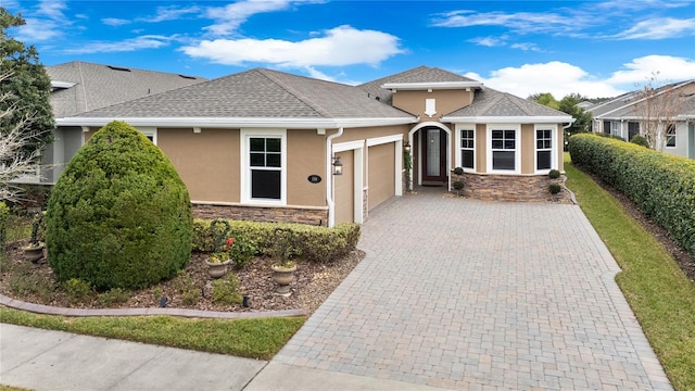 view of front of home featuring a garage, stone siding, decorative driveway, and stucco siding