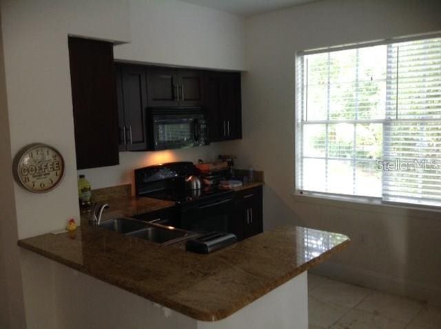 kitchen featuring light tile patterned floors, stone countertops, black appliances, and kitchen peninsula