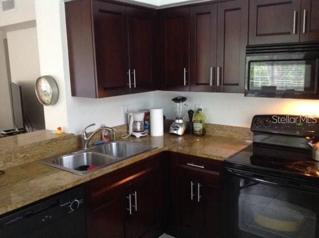 kitchen with light stone counters, black appliances, dark brown cabinets, and sink