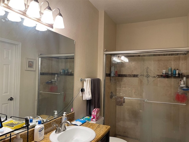 bathroom featuring a textured ceiling, walk in shower, vanity, and toilet