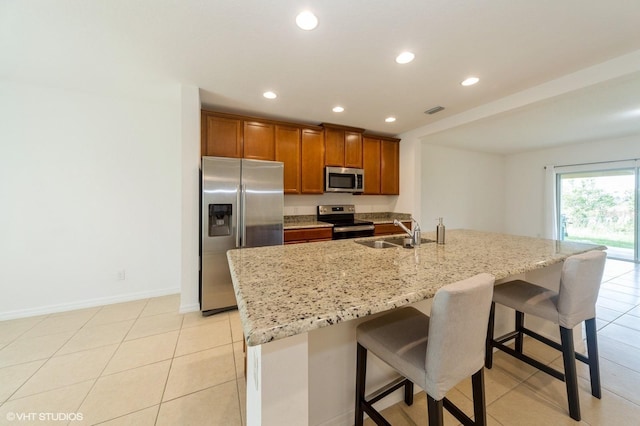 kitchen featuring sink, an island with sink, light stone countertops, a breakfast bar, and appliances with stainless steel finishes