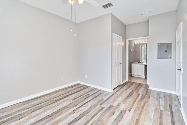 unfurnished bedroom featuring ceiling fan, electric panel, light hardwood / wood-style flooring, and ensuite bath