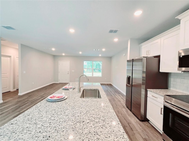 kitchen with stainless steel appliances, light stone counters, sink, white cabinetry, and backsplash