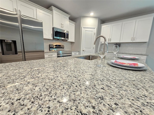 kitchen featuring sink, white cabinets, decorative backsplash, light stone countertops, and appliances with stainless steel finishes