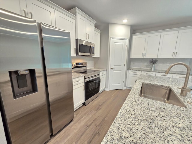 kitchen with stainless steel appliances, sink, white cabinets, light stone counters, and tasteful backsplash