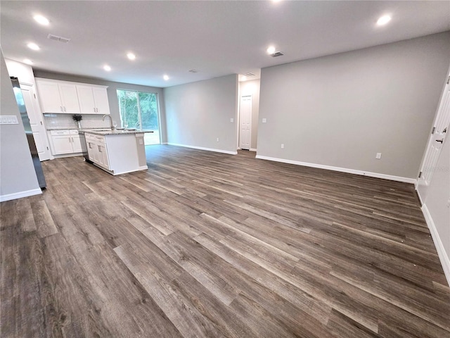 kitchen with a kitchen island with sink, dark wood-type flooring, decorative backsplash, white cabinets, and sink