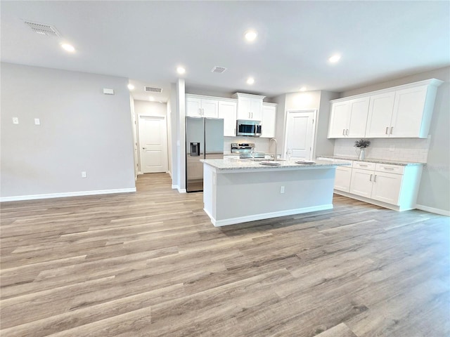 kitchen featuring light stone counters, a center island with sink, light hardwood / wood-style floors, white cabinets, and appliances with stainless steel finishes