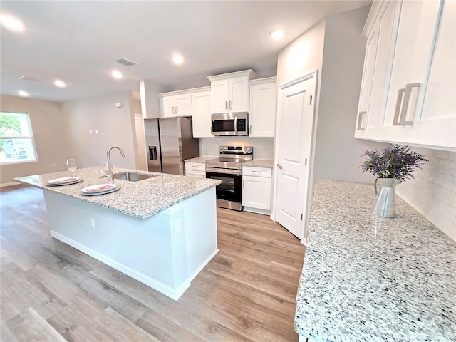 kitchen with light stone countertops, stainless steel appliances, a kitchen island with sink, white cabinetry, and sink