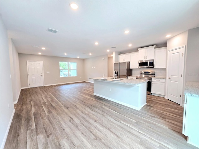 kitchen with stainless steel appliances, white cabinetry, light stone counters, light wood-type flooring, and an island with sink