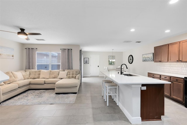 kitchen featuring pendant lighting, sink, backsplash, a kitchen island with sink, and ceiling fan