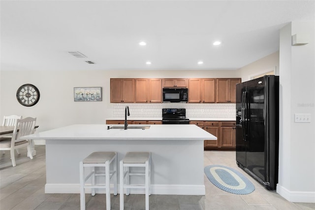 kitchen featuring sink, backsplash, a kitchen breakfast bar, black appliances, and a center island with sink