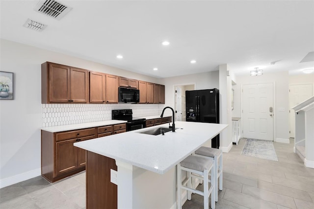 kitchen featuring sink, a breakfast bar area, black appliances, a center island with sink, and decorative backsplash