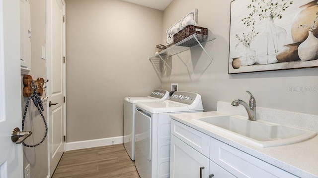 clothes washing area featuring sink, washing machine and dryer, cabinets, and light hardwood / wood-style flooring