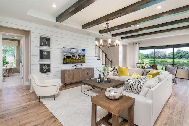 living room with a notable chandelier, light wood-type flooring, wood walls, and beam ceiling